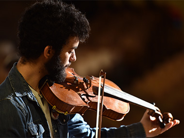 Student playing violin, wearing a denim jacket.