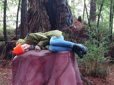 Photo of student laying on artist's tree stump installation